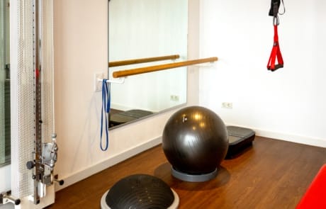 Eine Fitnessecke mit Spiegel, Widerstandsbändern, Kabelzugmaschine, Bosu-Ball, Gymnastikball, TRX-Bändern und Holzboden.