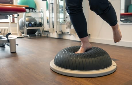 Person, die in einem Fitnessstudio auf einem Gleichgewichtstrainer auf einem Bein balanciert.