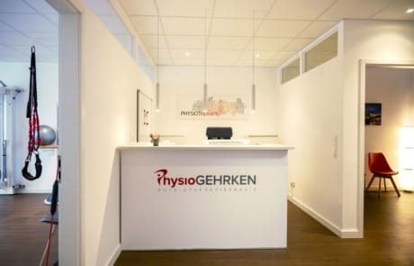 Ein moderner Empfangsbereich für Physiotherapie mit einem weißen Schreibtisch, Branding auf der Vorderseite, einem Stuhl im Hintergrund und Trainingsgeräten an der Seite.