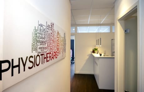 Ein Flur in einer Physiotherapieklinik mit einem Wortwolken-Kunstwerk an der Wand und einem Empfangstresen im Hintergrund.