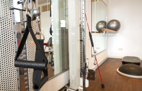 Ein Fitnessstudio mit Trainingsgeräten wie Widerstandsbändern, Balancebällen und einer Kabelmaschine in einem verspiegelten Raum.